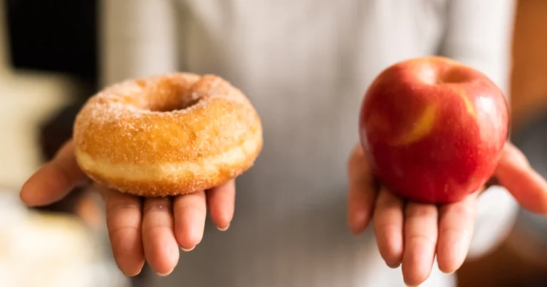 Une femme tient une pomme un aliment bruts et un beignet un aliment ultra transformés.
