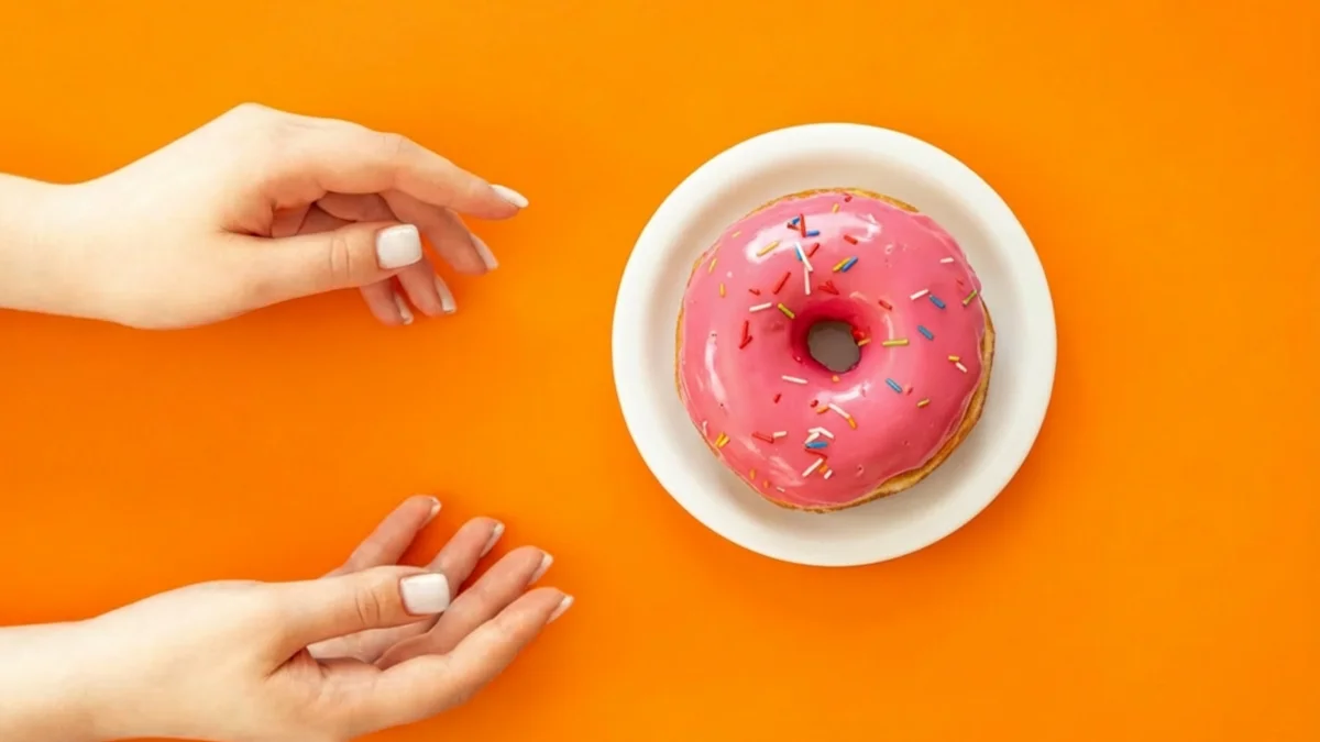 Mains tentées par un donut illustrant les envies de sucre contrôlées par le microbiote