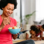 Femme mangeant une salade de fruits et légumes après une séance d'activité physique à la maison, alimentation saine et sport pour la prévention du cancer