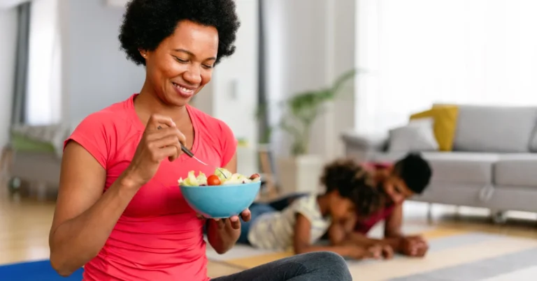 Femme mangeant une salade de fruits et légumes après une séance d'activité physique à la maison, alimentation saine et sport pour la prévention du cancer